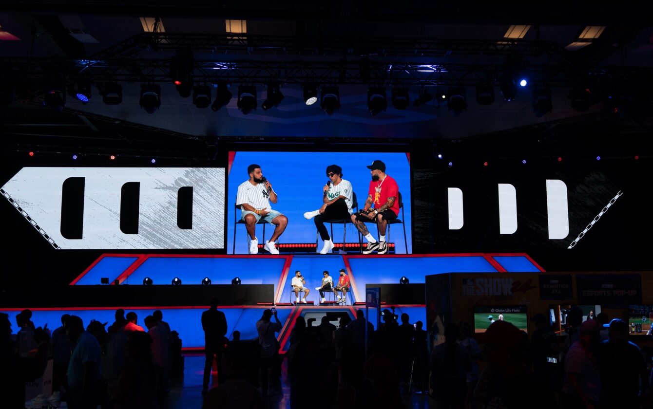 MLB All-Star Village 2024 Texas live event programming with panel discussion, stage lighting, large video display, and crowd gathered in front